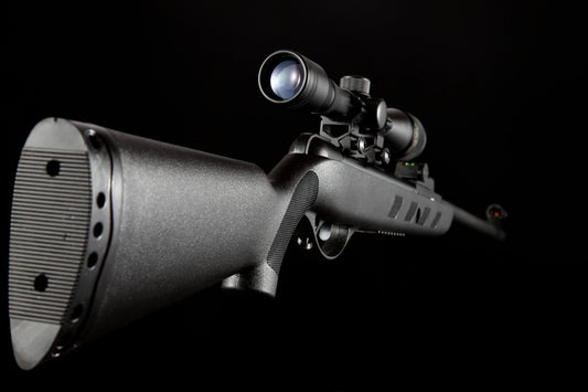 Black air rifle with mounted scope isolated on black background, side close-up view