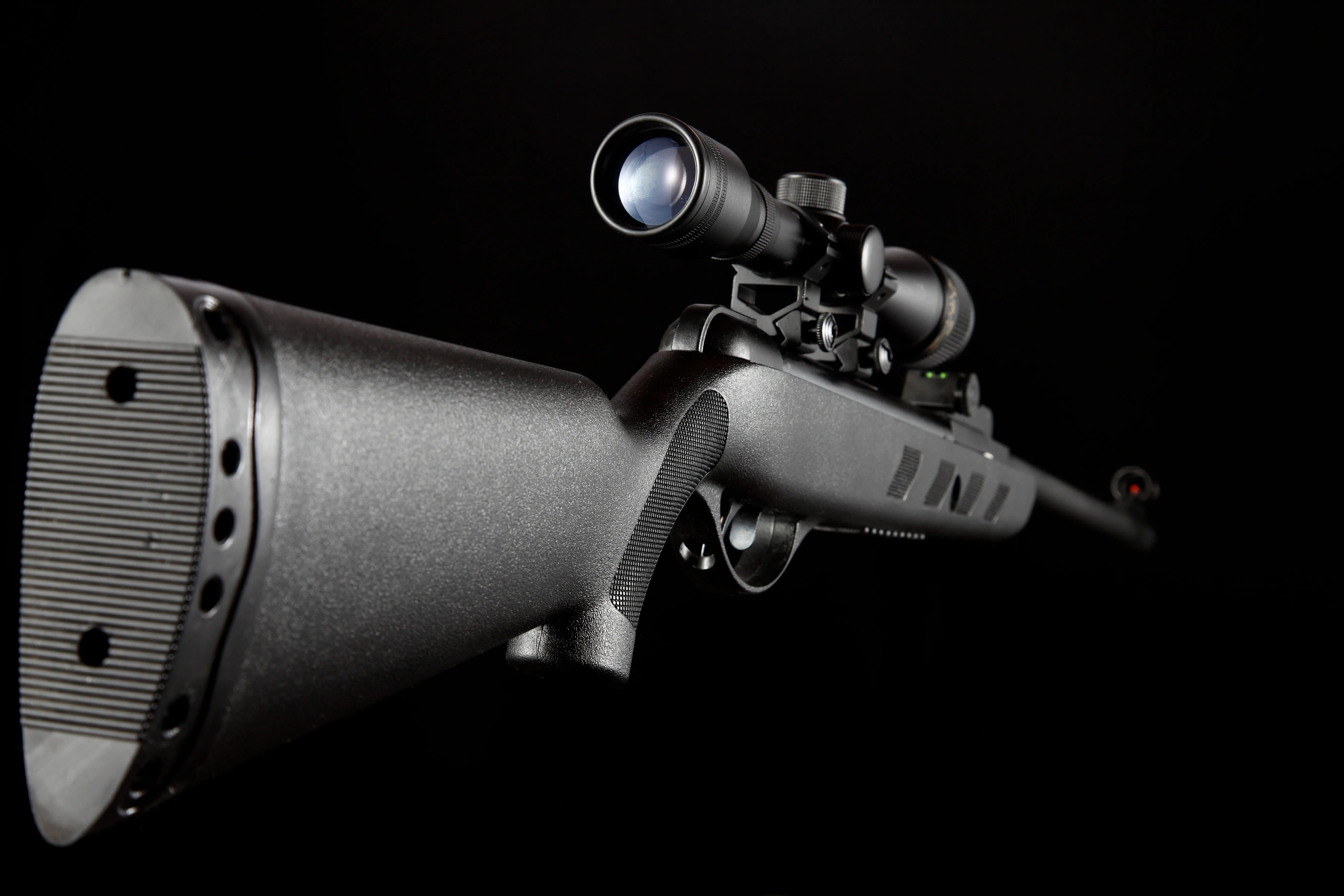 Black air rifle with mounted scope isolated on black background, side close-up view