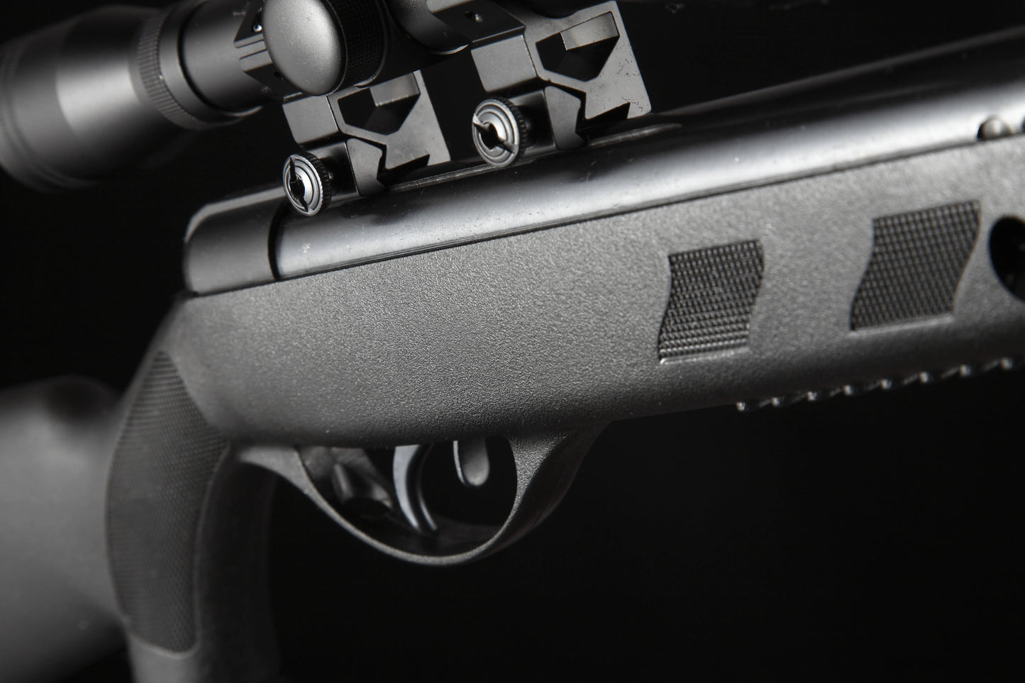 Close-up of a black air rifle trigger and scope mount with textured grip