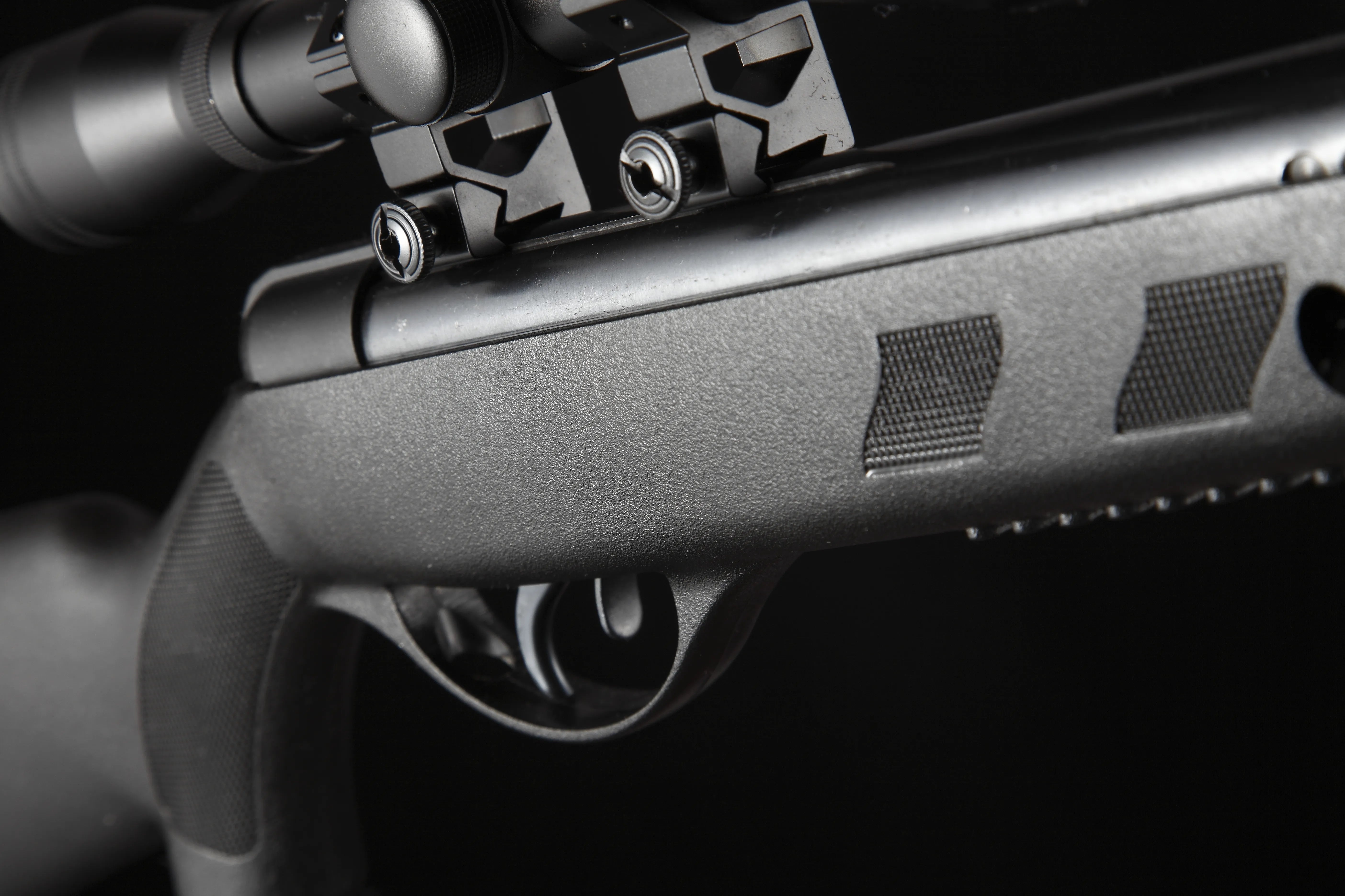 Close-up of a black air rifle trigger and scope mount with textured grip