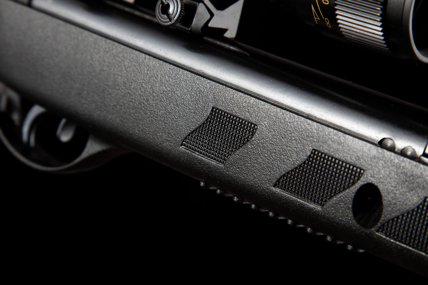 Close-up of textured black air rifle body with trigger and scope adjustment dial