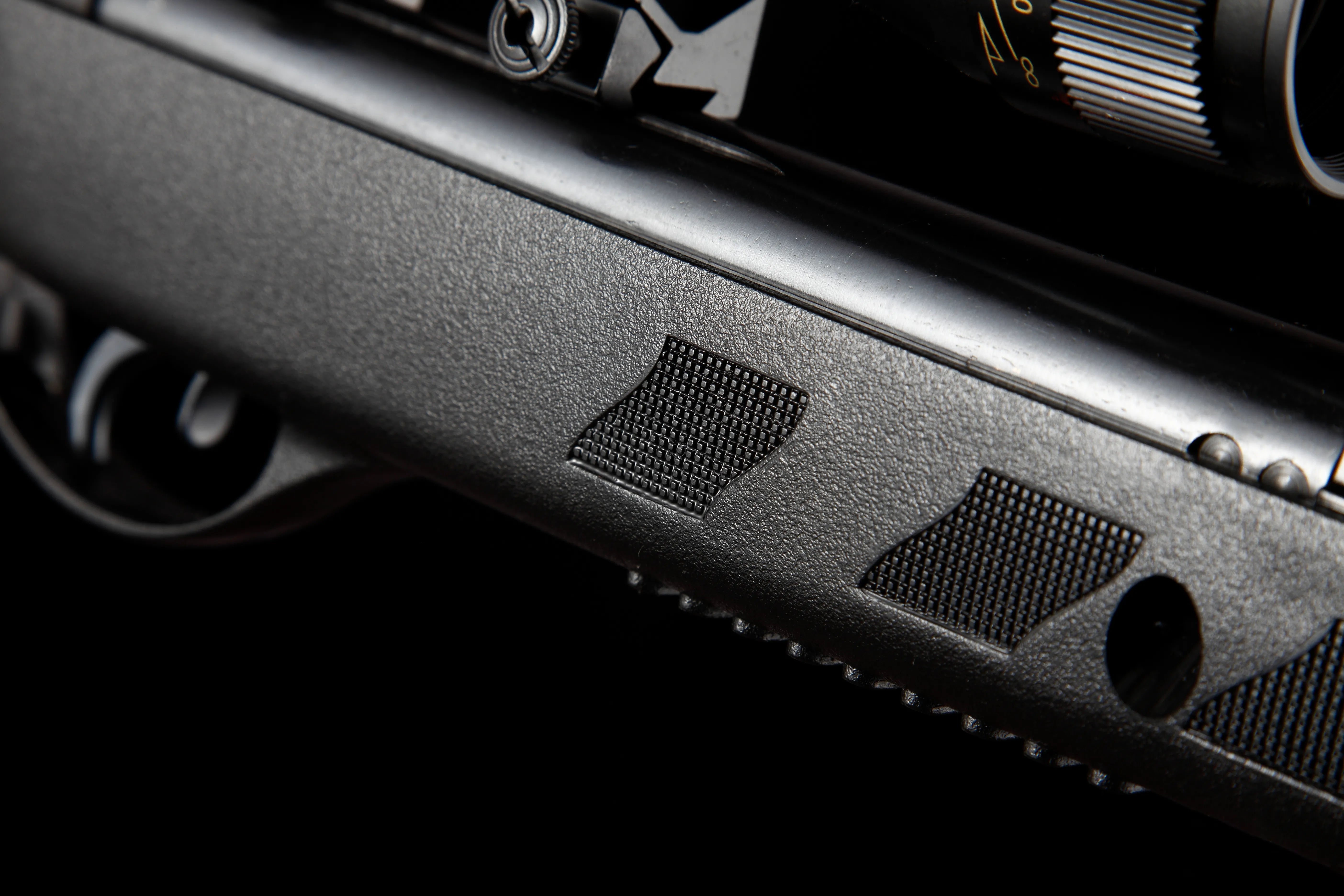 Close-up of textured black air rifle body with trigger and scope adjustment dial